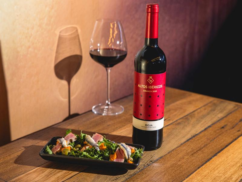 Bottle of Altos Ibéricos Crianza 2020 Rioja red wine with a glass and Spanish anchovy salad, photographed at OLÉ Restaurant in South Bank, Brisbane.
